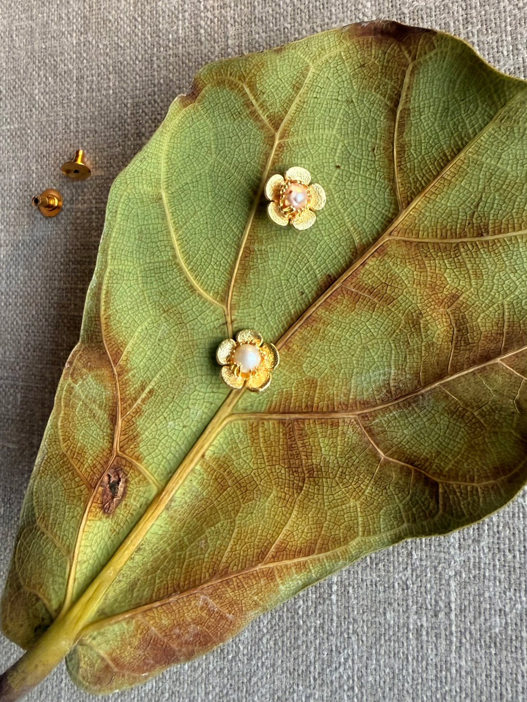 Gold floral earrings on a large green leaf with a gray background