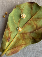 Gold floral earrings on a large green leaf with a gray background