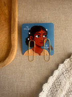 Taar earrings on a card with a woman's face illustration, placed on a textured surface.