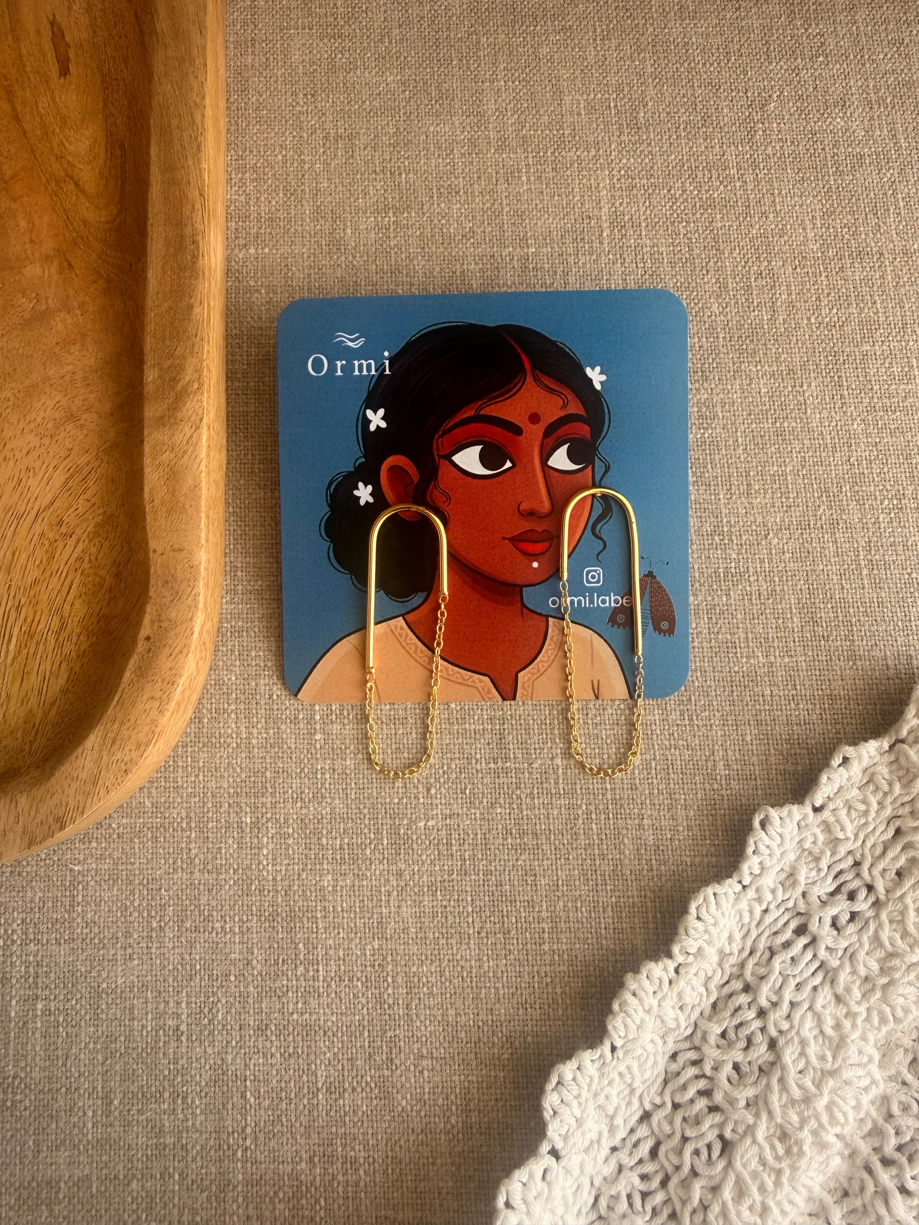 Taar earrings on a card with a woman's face illustration, placed on a textured surface.
