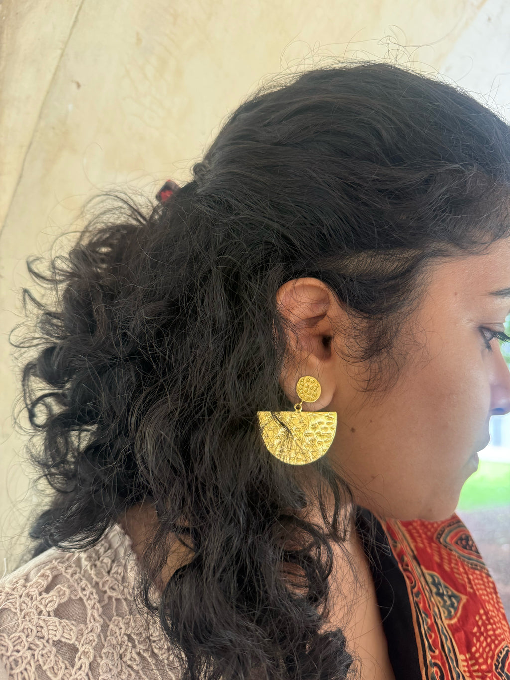 Close-up of a woman wearing gold plated earrings with a neutral background