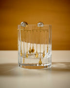 Clear glass holder with baroque pearl and gold color dangling earrings on a mustard background