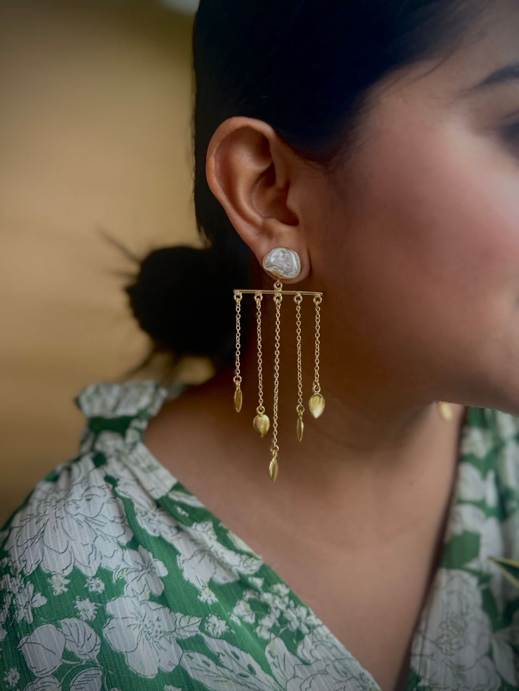Close-up of a woman wearing gold earrings with dangling elements, blurred background