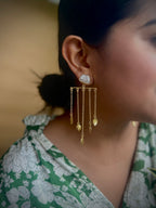 Close-up of a woman wearing gold earrings with dangling elements, blurred background