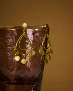 Close up of Gold earrings with dangling elements on a reflective glass against a mustard color background