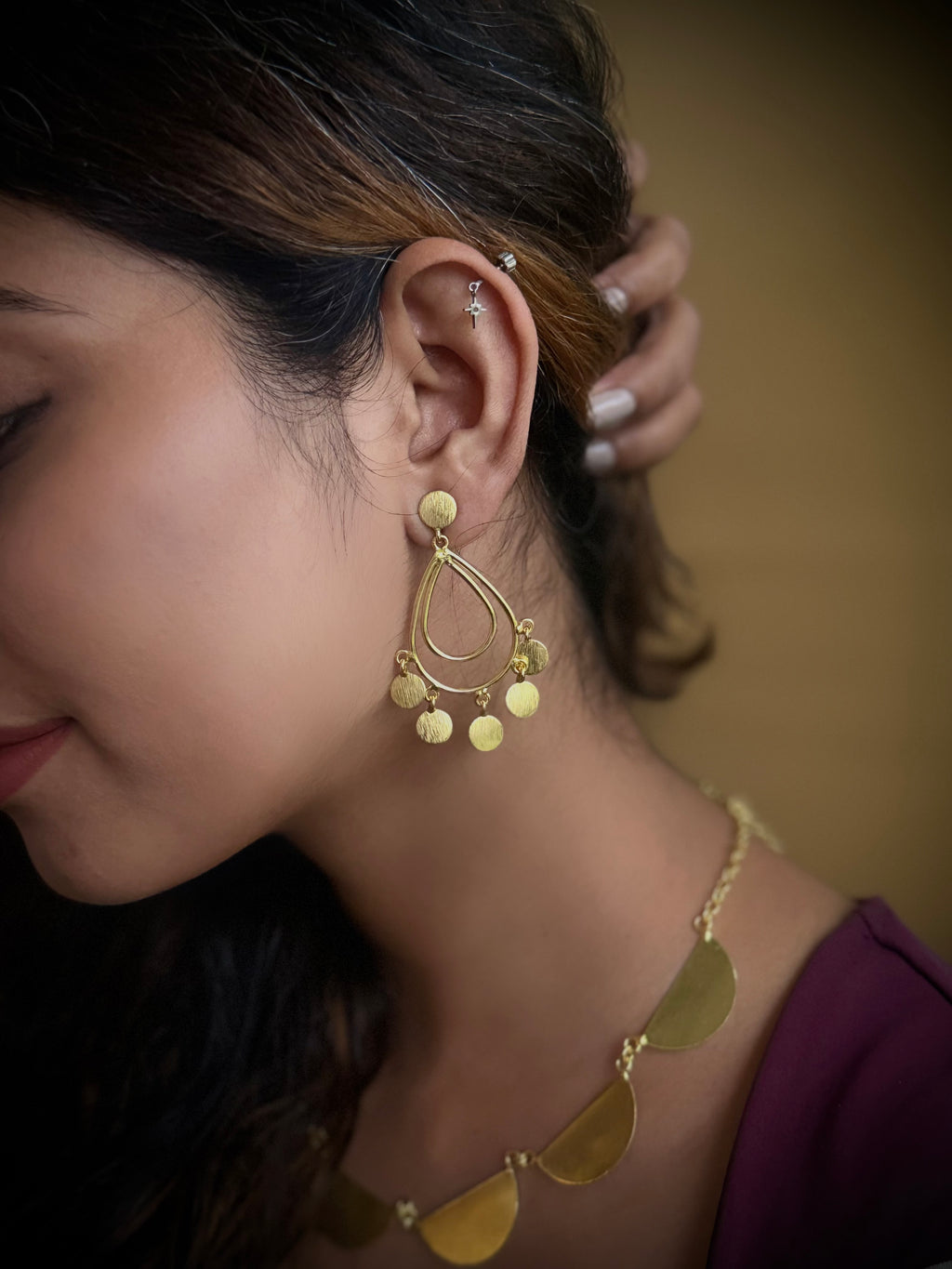 Woman wearing gold earrings and necklace against a blurred background
