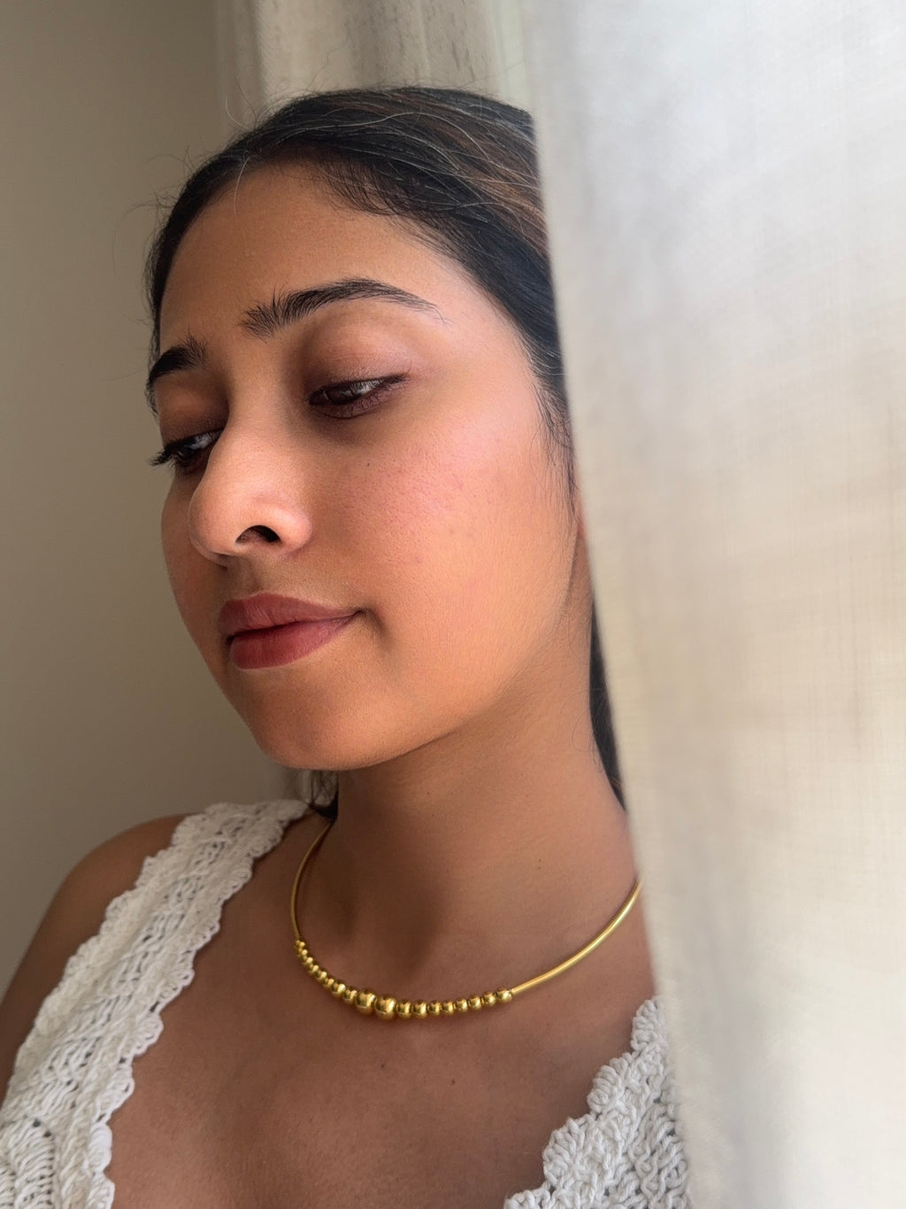 Close-up of woman wearing the Kanak choker, gold beaded cluster resting at the centre of the neck, white crochet top, soft natural light