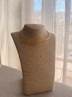 Gold necklace on a brown mannequin bust against a sheer curtain background