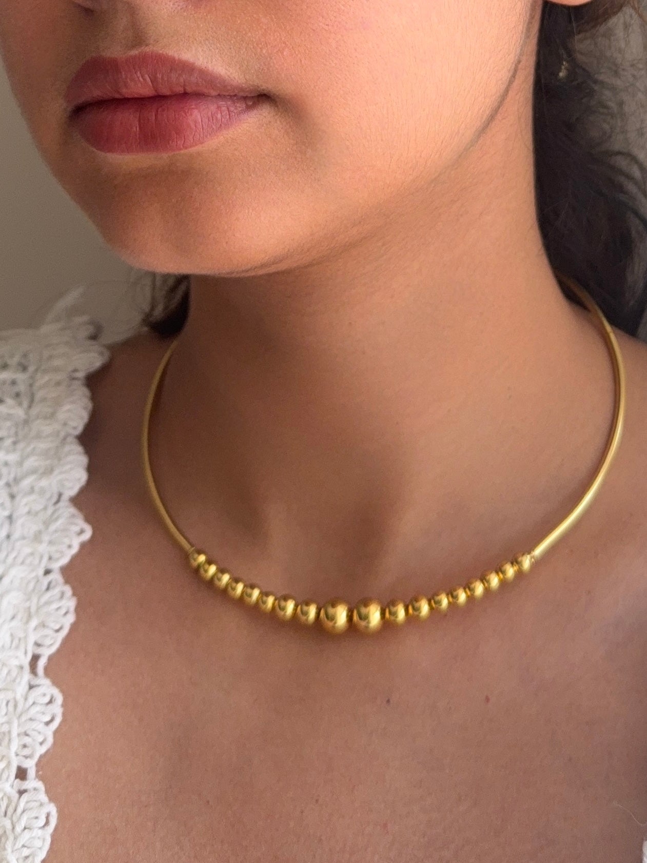 Close-up of a person wearing a gold necklace with a neutral background