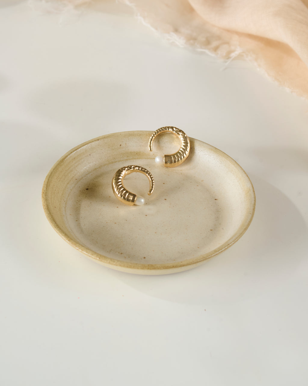 Beige ceramic dish with pearl gold plated earrings on a white background
