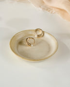 Beige ceramic dish with pearl gold plated earrings on a white background