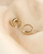 Close up of pearl gold plated earrings on a light beige fabric.