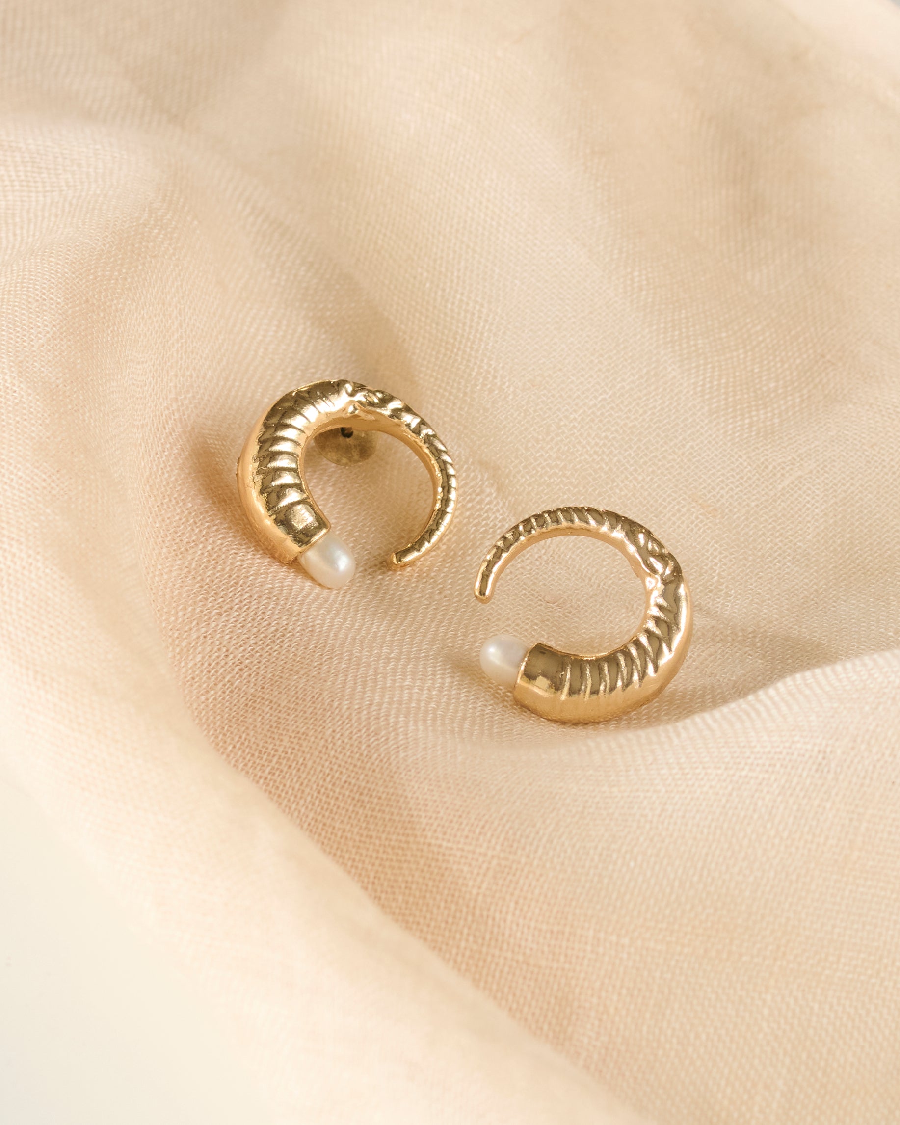 Close up of pearl gold plated earrings on a light beige fabric.