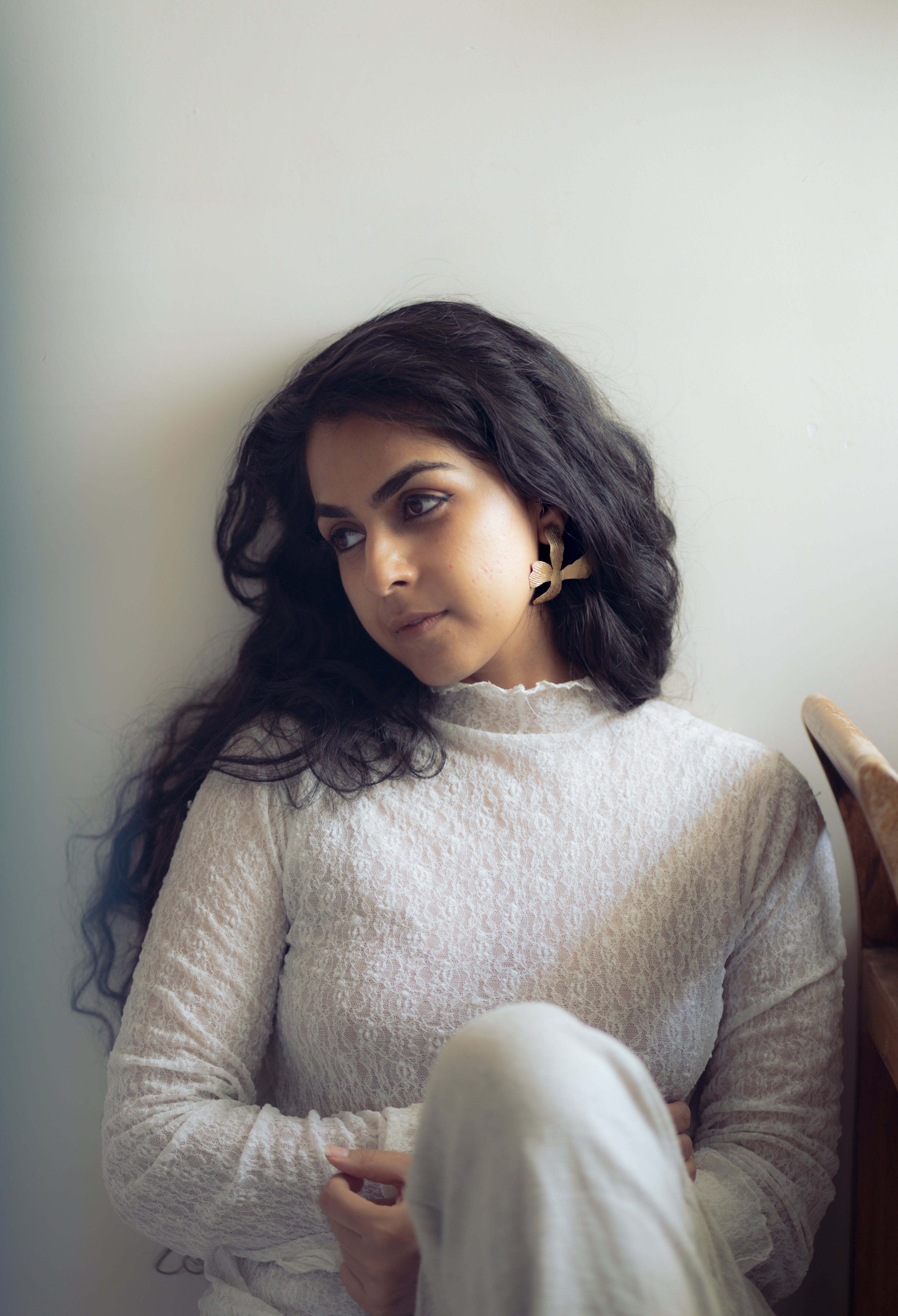Closeup of Woman in a white textured top and white cotton pants, sitting against a light background, wearing komal floret earrings.