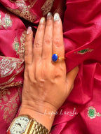 Lapis Lazuli ring with an oval deep blue stone in a gold setting, worn on a hand resting on pink silk