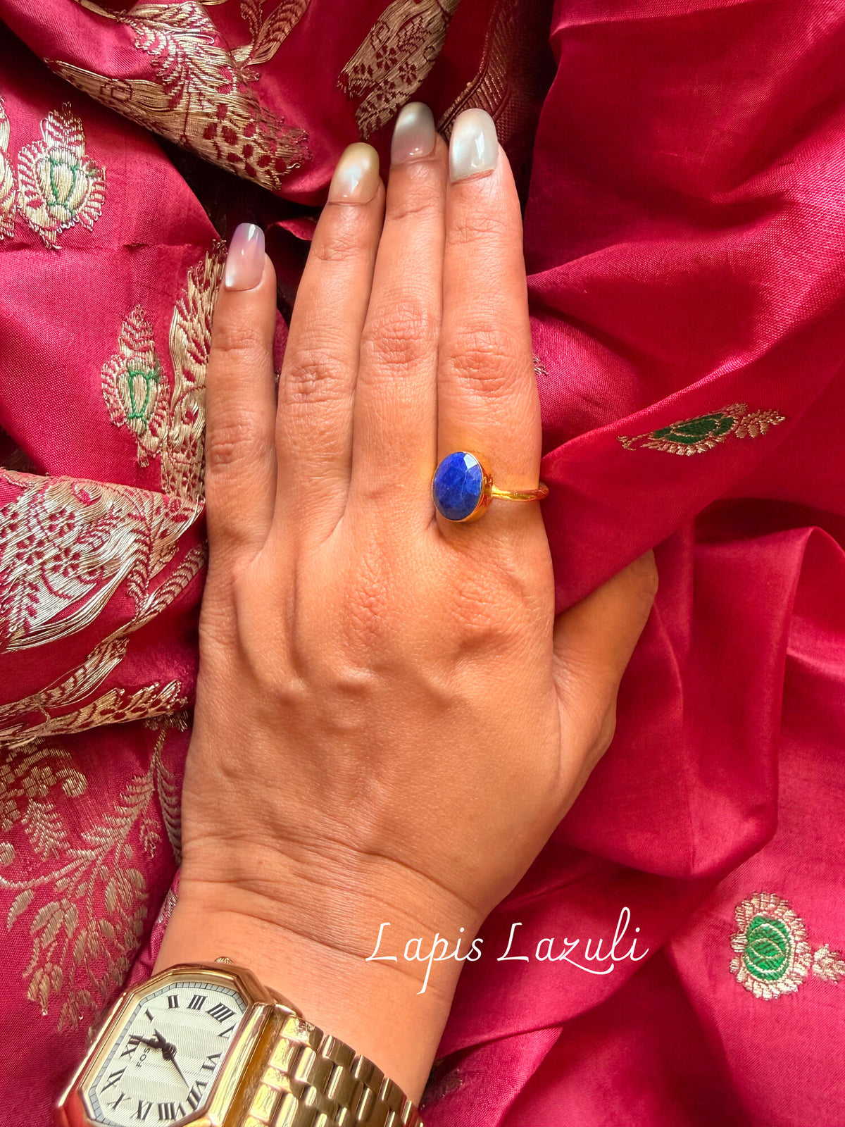 Lapis Lazuli ring with an oval deep blue stone in a gold setting, worn on a hand resting on pink silk