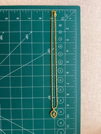 Full length flat lay of the Lily Necklace on a green cutting mat with ruler, showing the complete barrel-link chain length and oval lily pendant at approximately 10 inches.