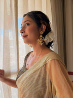 Woman in a gold sheer saree looking out of a sunlit window, wearing Malika Danglers with a white flower in her hair