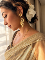 Side profile of a woman in a sequinned gold saree wearing a Malika Dangler, with a white fabric flower in her hair and a fine gold necklace
