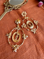 Malika Danglers laid on rust linen with the earring back showing, beside an antique brass hand mirror and a dried pink flower