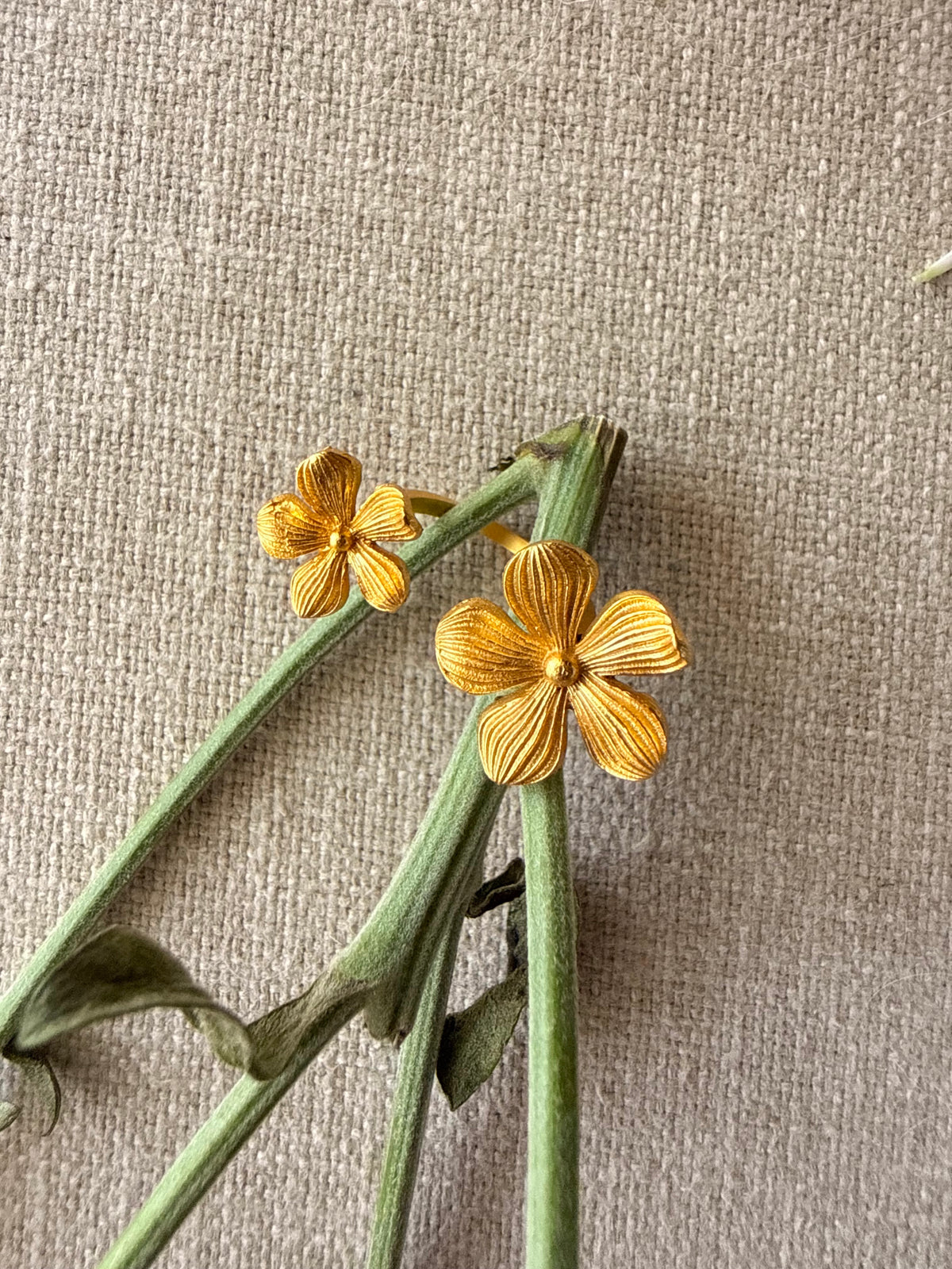 Close-up shot of the gold toned Manjari Ring resting on fresh green flower stems against a neutral textured fabric background.