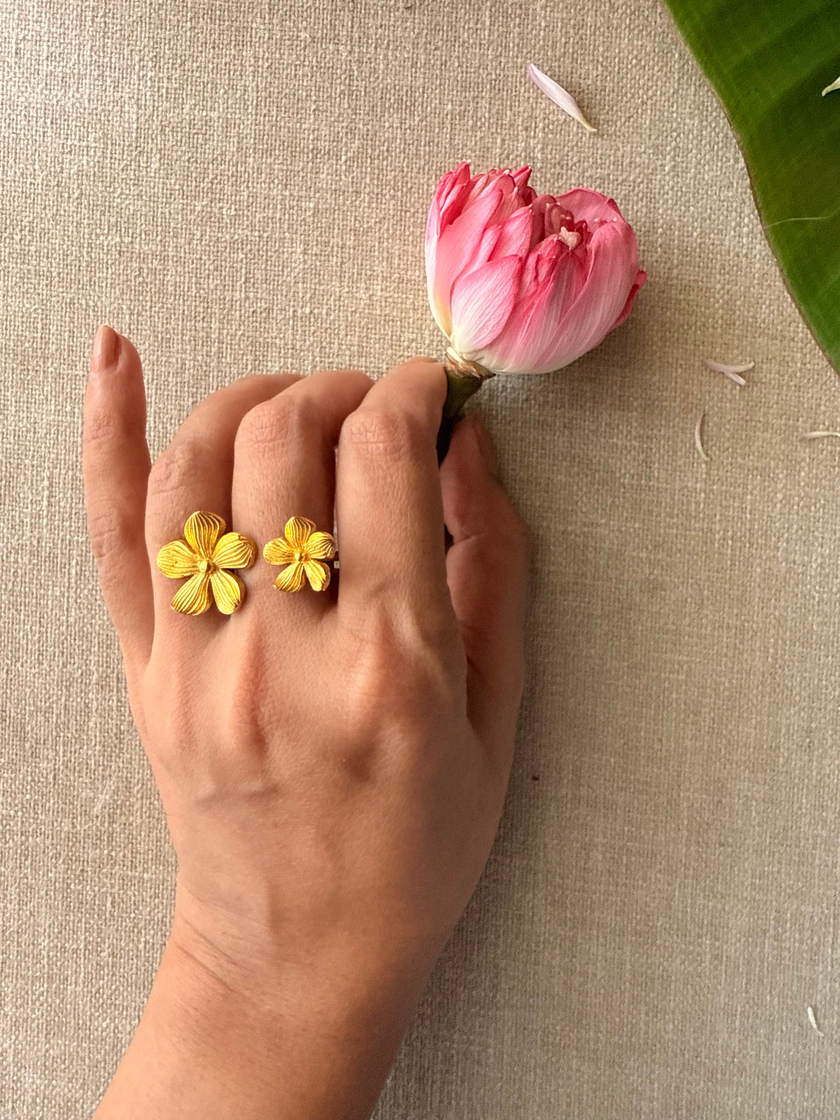 A model wearing the gold Manjari Ring on her index finger while delicately holding a pink lotus bud.