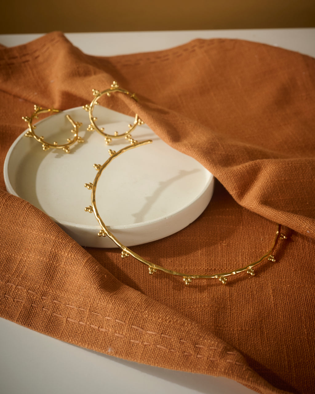 Gold hoop earrings and circular chocker on a white dish with brown fabric