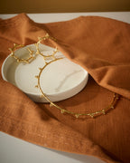 Gold hoop earrings and circular chocker on a white dish with brown fabric