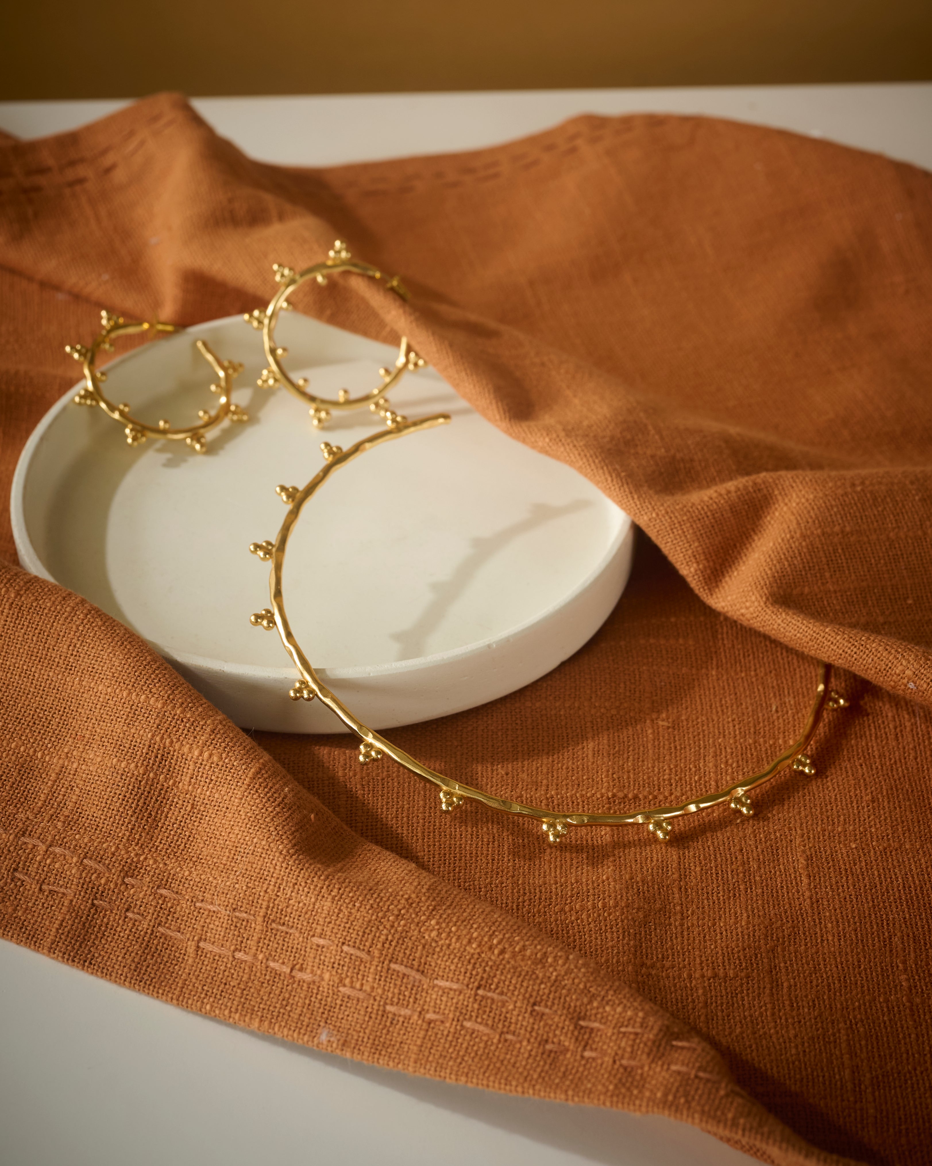 Gold hoop earrings and circular chocker on a white dish with brown fabric