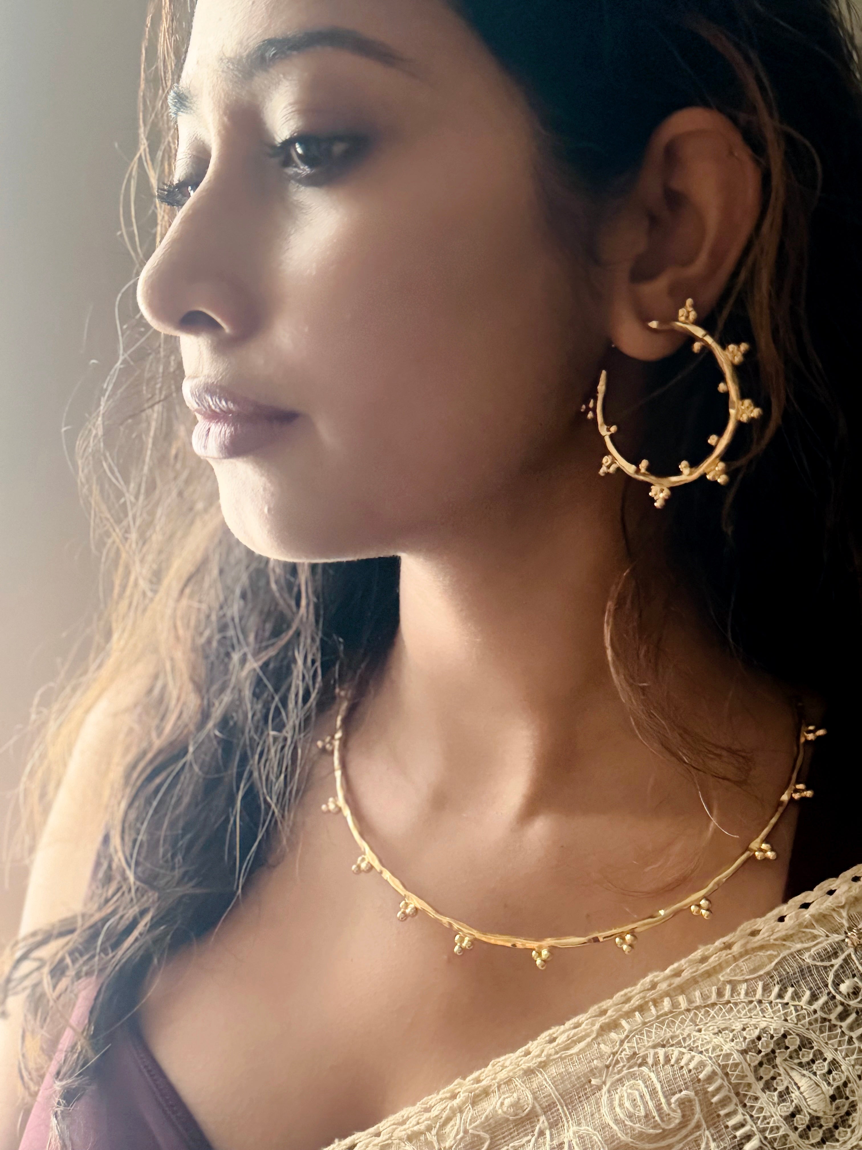 Woman wearing gold hoop earrings and matching chocker, close-up of face and neck.
