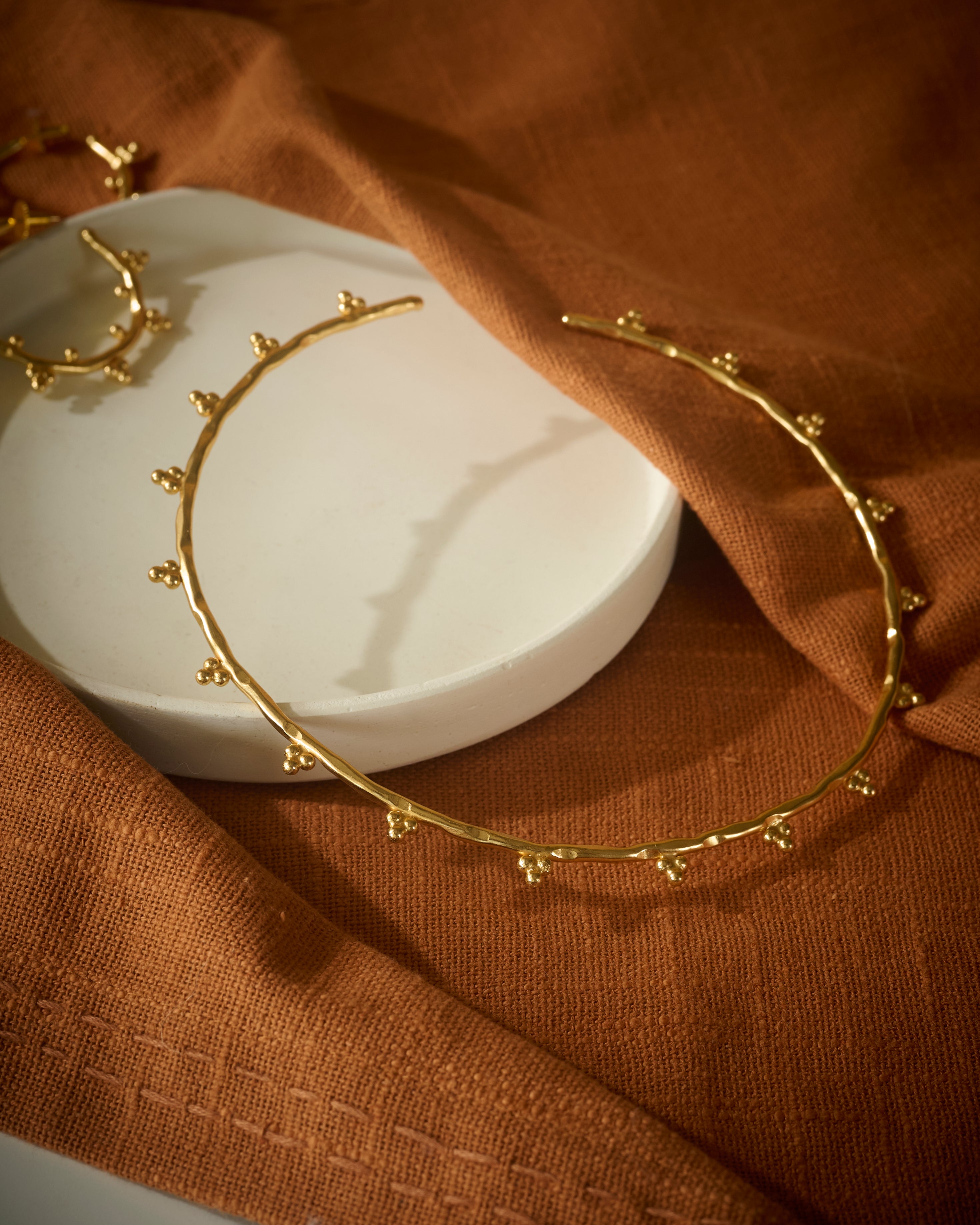 Gold circular chocker on a white dish with a brown fabric background