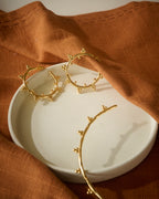 Gold hoop earrings on a white dish with a brown fabric background