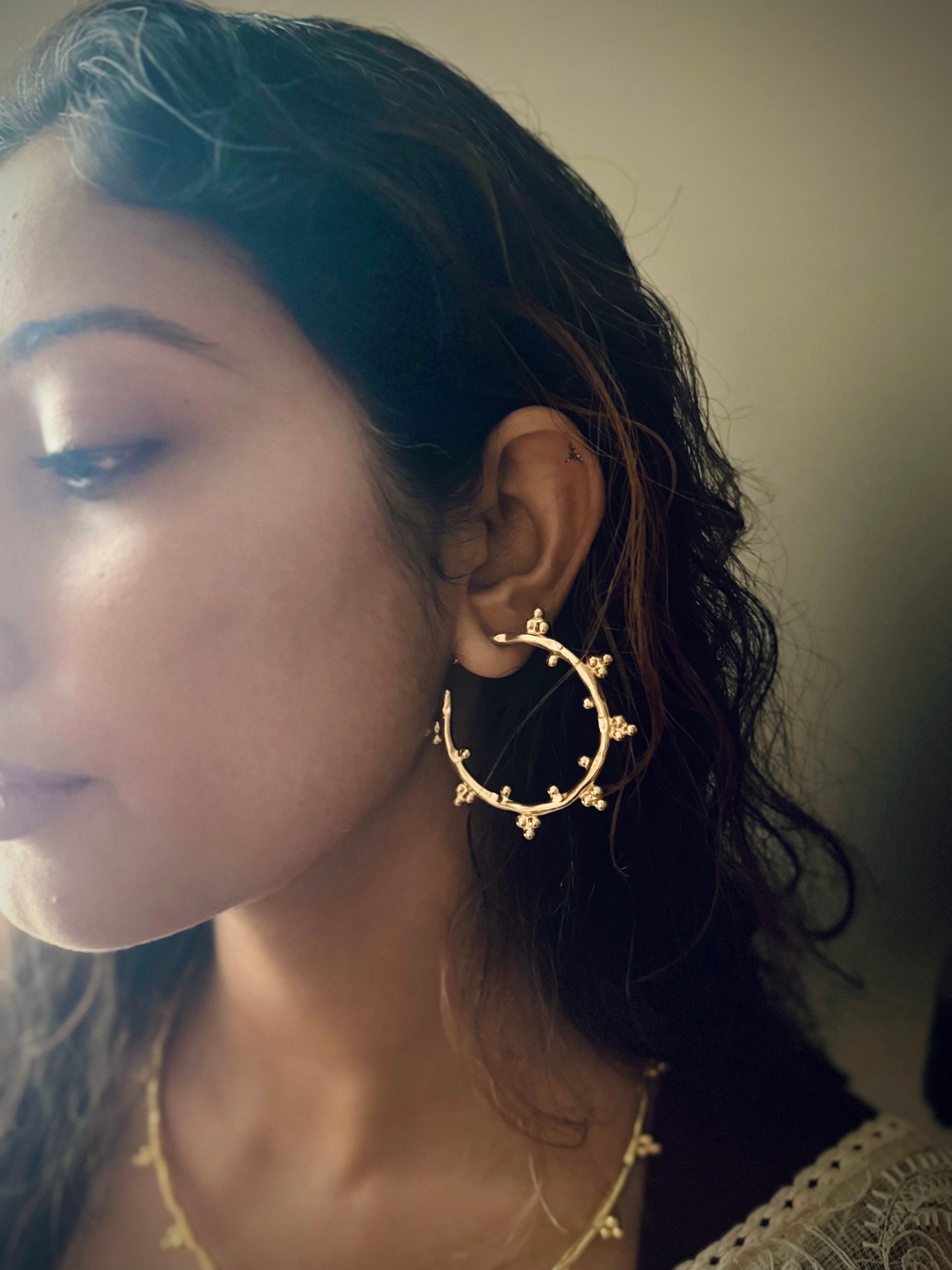 Close-up of a woman wearing gold hoop earrings with a neutral background