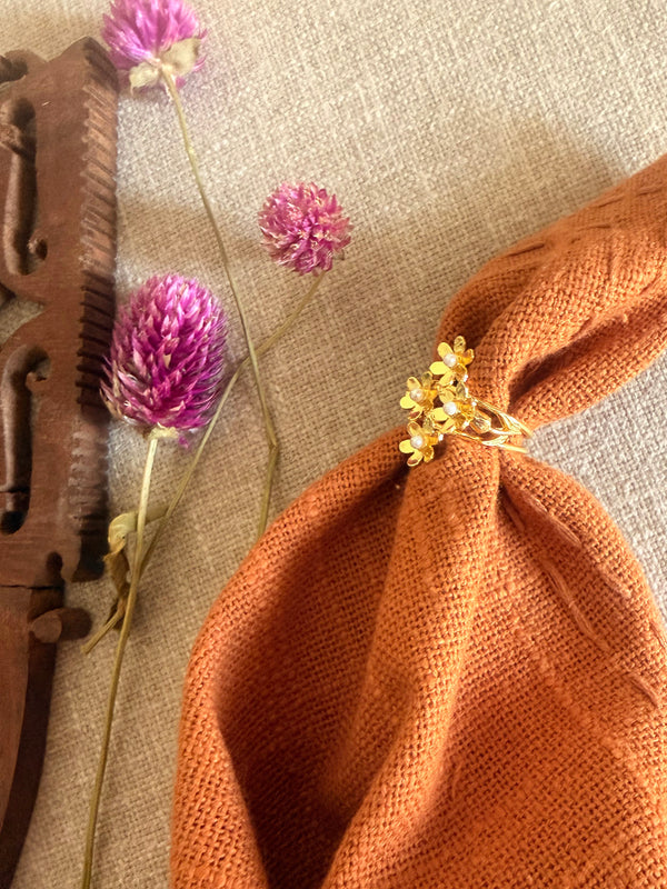 Gold plated brass Motiya Lily Ring with jasmine flower cluster and pearl centres displayed on a gathered terracotta linen cloth, surrounded by dried purple globe amaranth flowers and a vintage wooden carved block on natural linen texture.