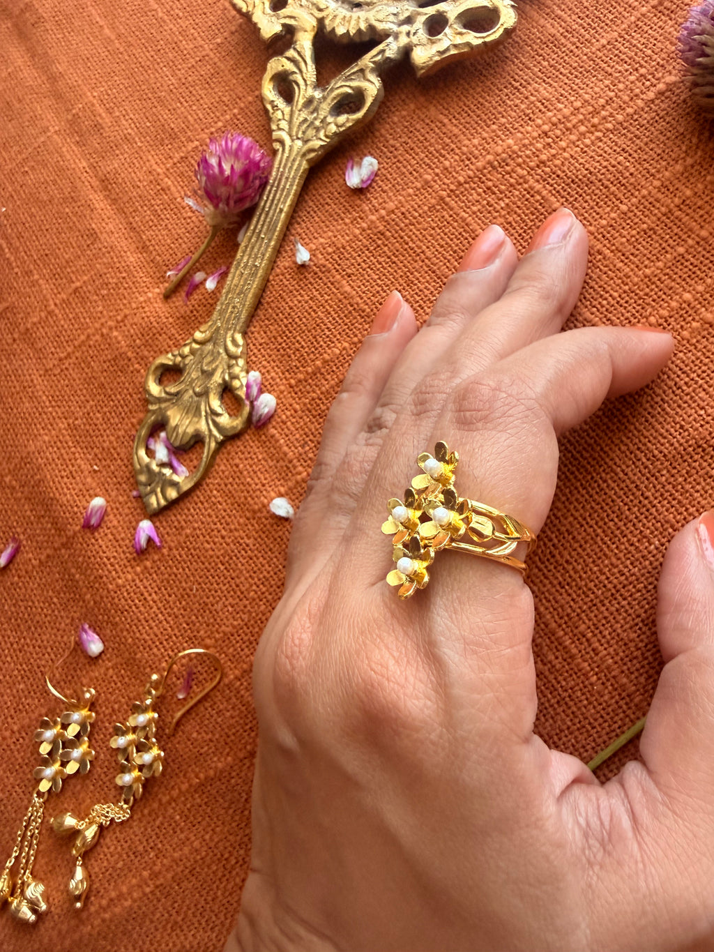 Close overhead shot of Motiya Lily Ring on the hand against terracotta linen.