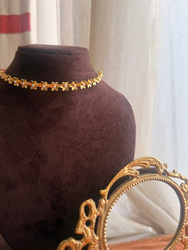 Gold plated brass Motiya Choker with tiny jasmine-shaped flowers and pearl centres, displayed on a dark velvet bust with a vintage gold mirror in the foreground.