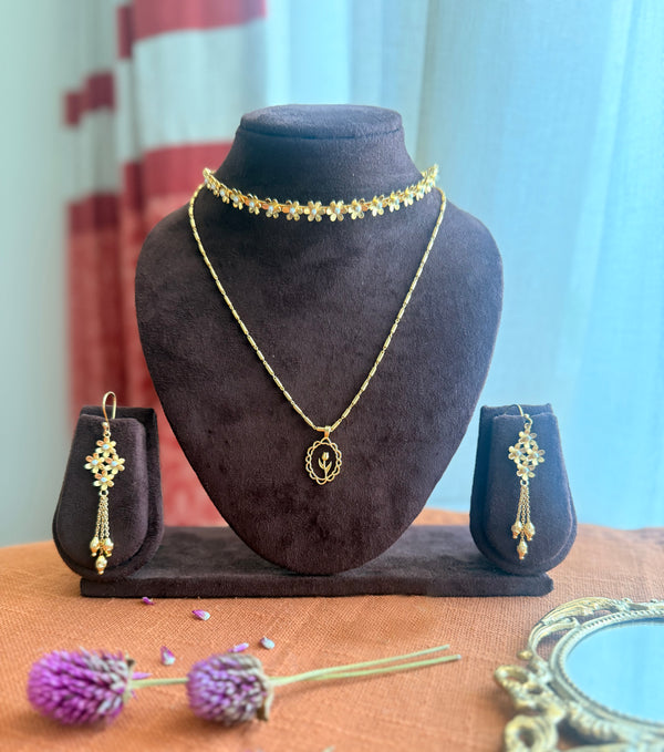 Motiya Essentials set displayed together — Motiya Choker and Lily Necklace layered on a dark velvet bust, Motiya Danglers on small velvet stands on either side, styled with dried purple globe amaranth flowers and a vintage brass mirror on terracotta linen, with soft natural light and red striped curtains in the background.