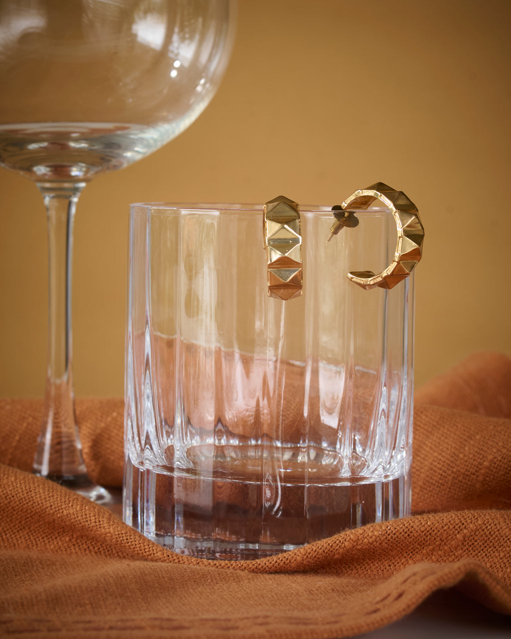 Edgy gold plated brass hoop earrings kept on a shiny glass.
