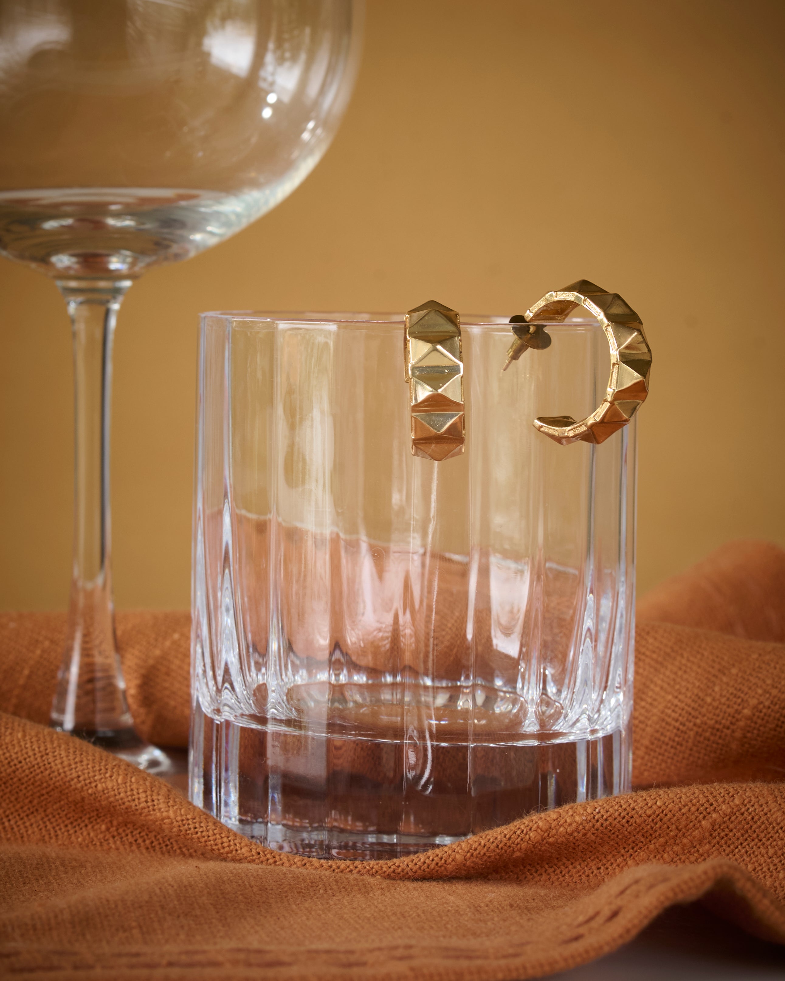 Edgy gold plated brass hoop earrings kept on a shiny glass.