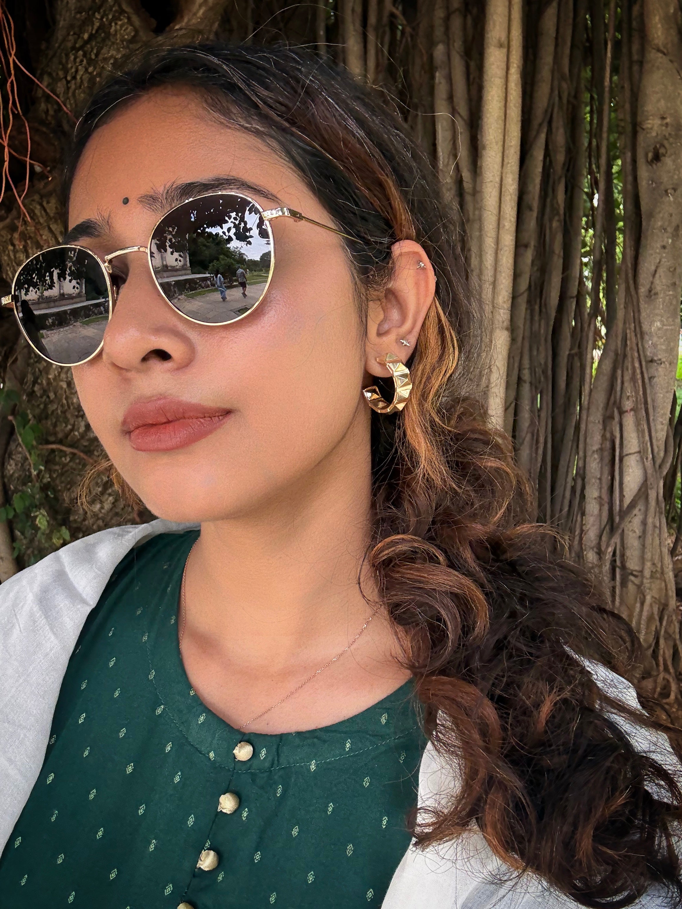 Woman wearing gold plated geometric hoop earrings with a natural background