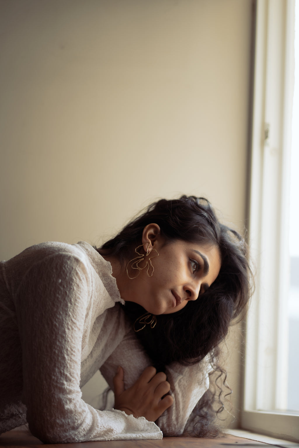 Woman with long hair sitting by a window, wearing Naksh Floral Earrings in soft lighting.