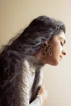 Woman with long hair sitting by a window, wearing Naksh Floral Earrings.