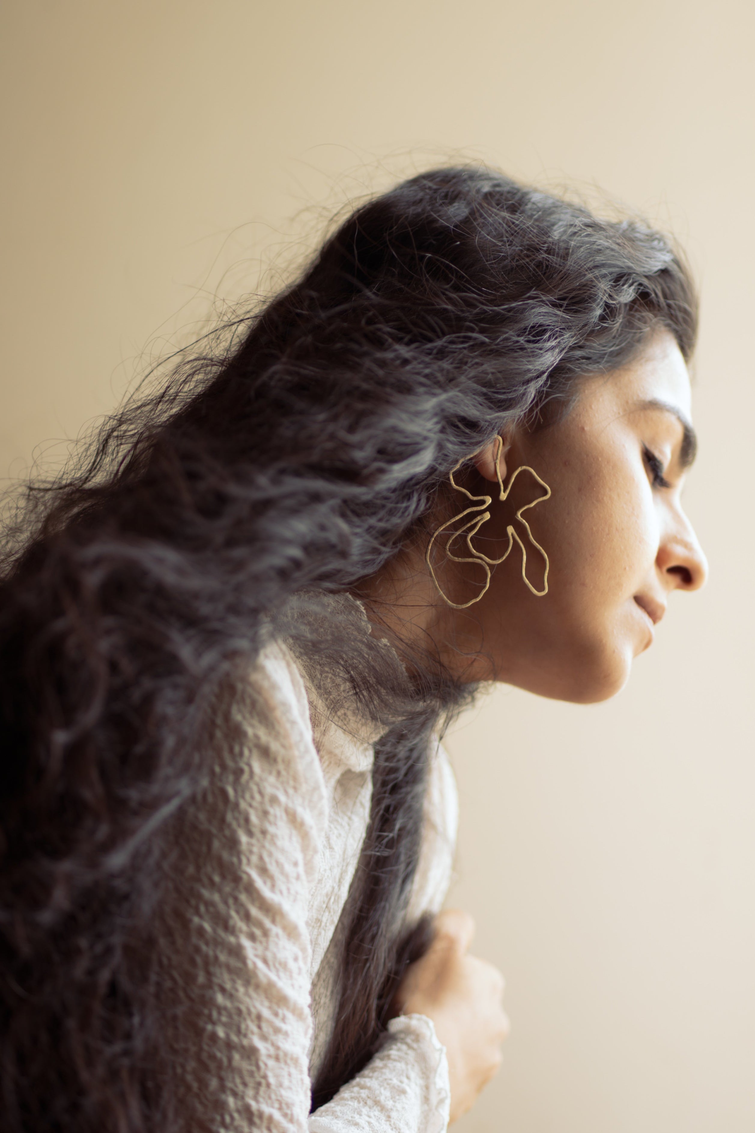 Woman with long hair sitting by a window, wearing Naksh Floral Earrings.