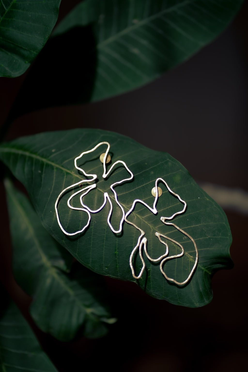 Naksh Floral Earrings on a green leaf with a dark background