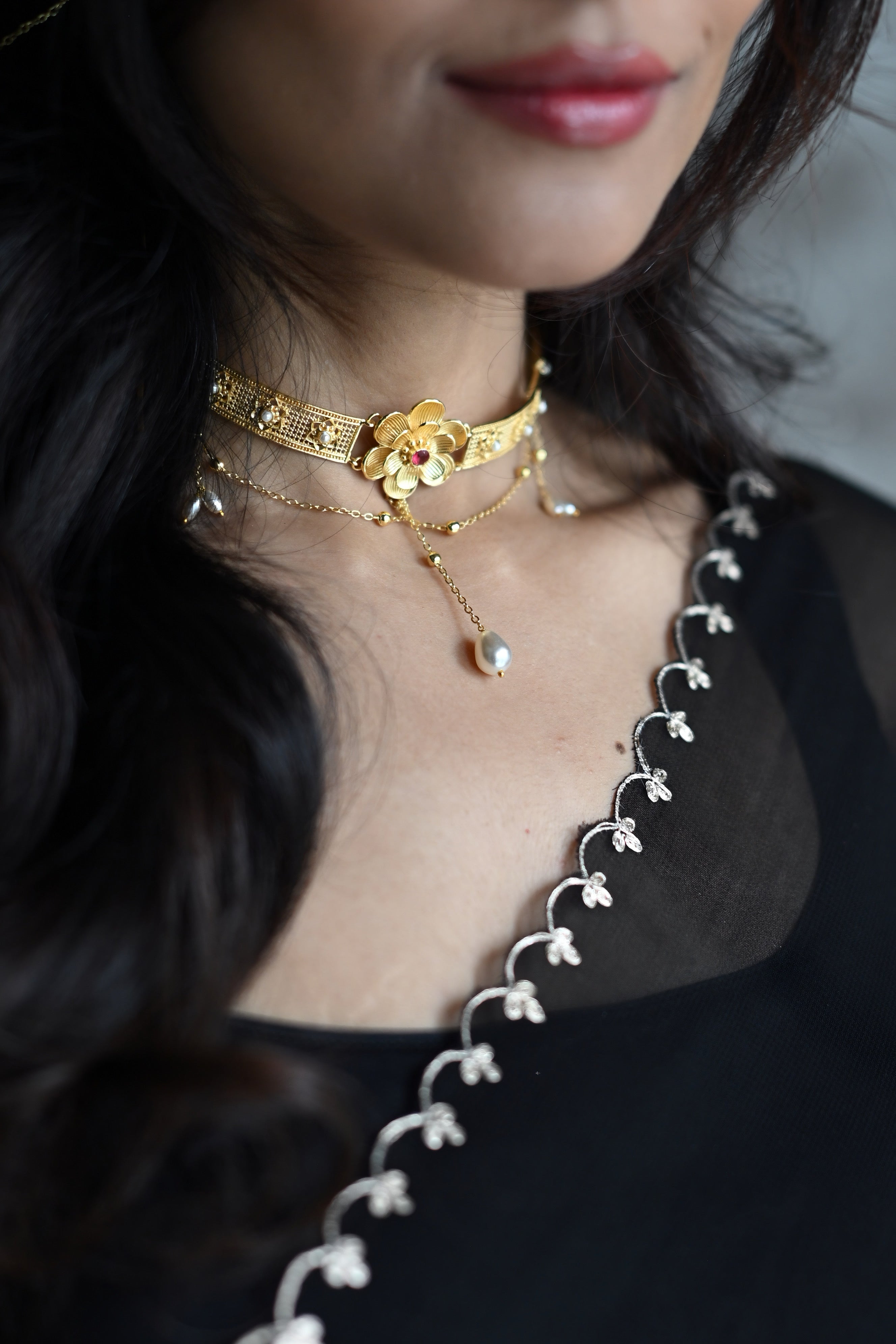 Close-up of woman wearing Nargis Choker against black outfit, gold flower centrepiece with ruby-coloured stone visible at the throat, pearl chain trailing down