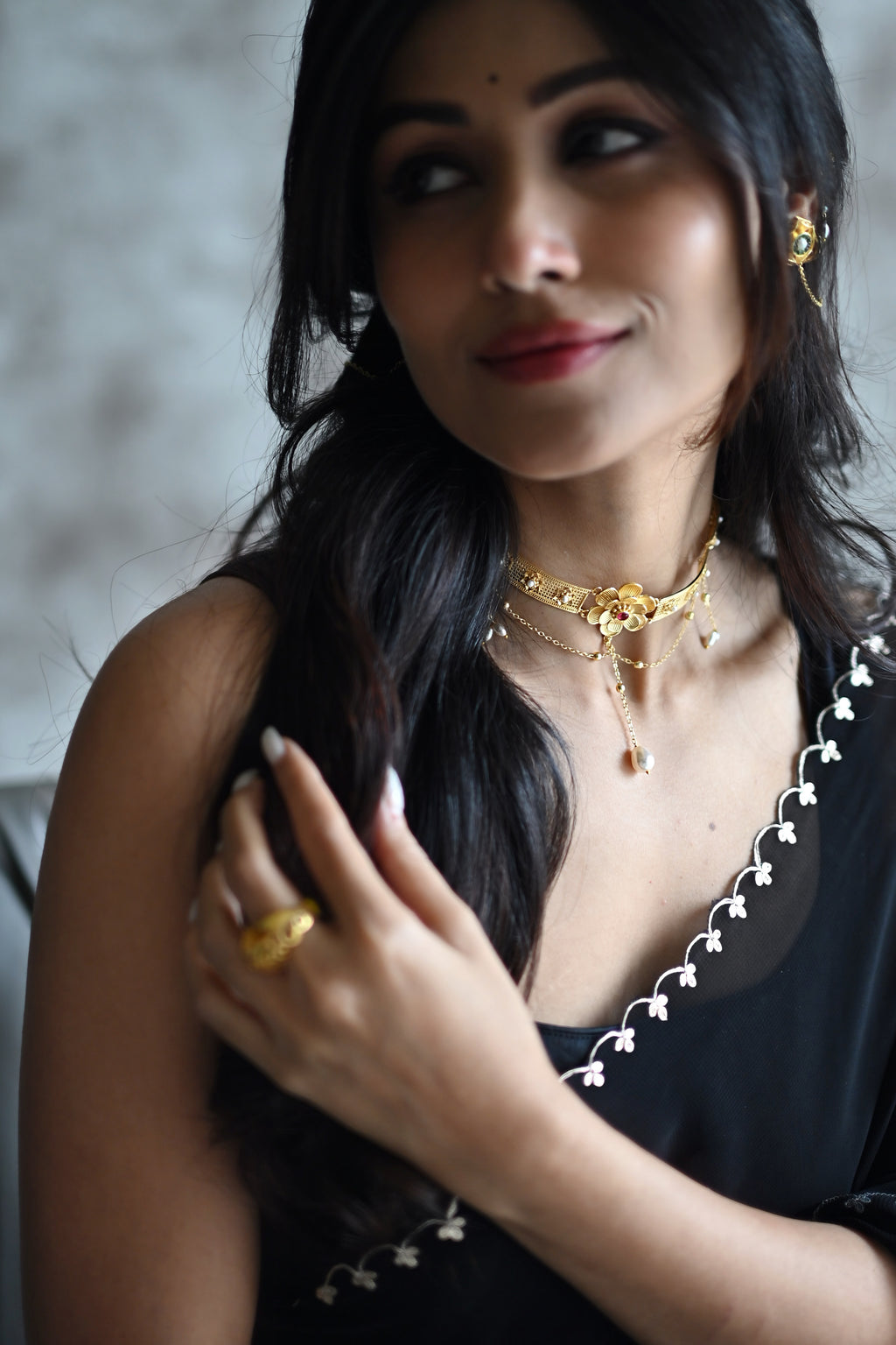 Woman wearing Nargis Choker and matching ring, looking over her shoulder, black outfit with pearl detailing, soft warm lighting