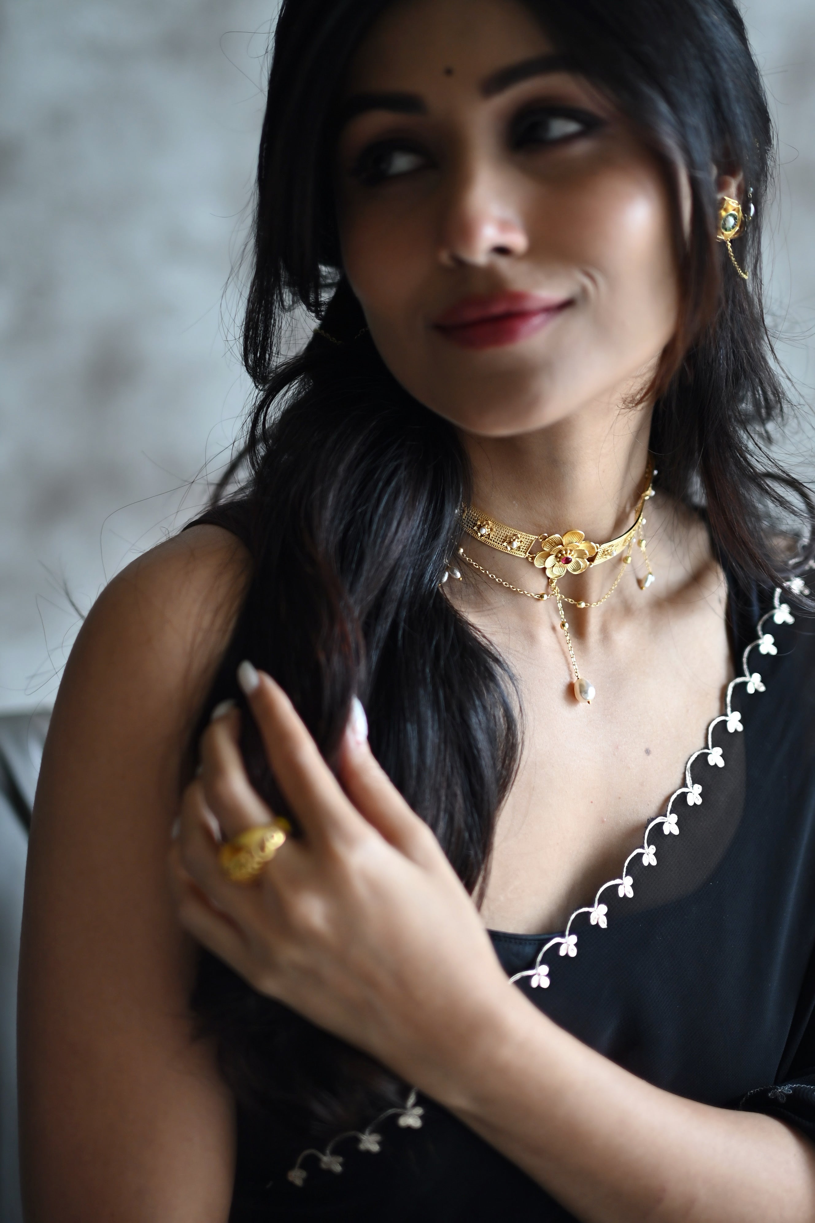 Woman wearing Nargis Choker and matching ring, looking over her shoulder, black outfit with pearl detailing, soft warm lighting