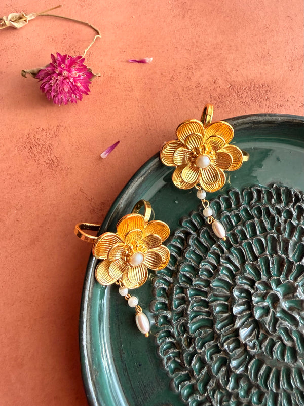 Nargis Ear Cuffs resting on a dark green ceramic tray on terracotta surface, gold ridged flower with pearl centre and pearl drop detail, dried pink Globe Amaranth flowers scattered around