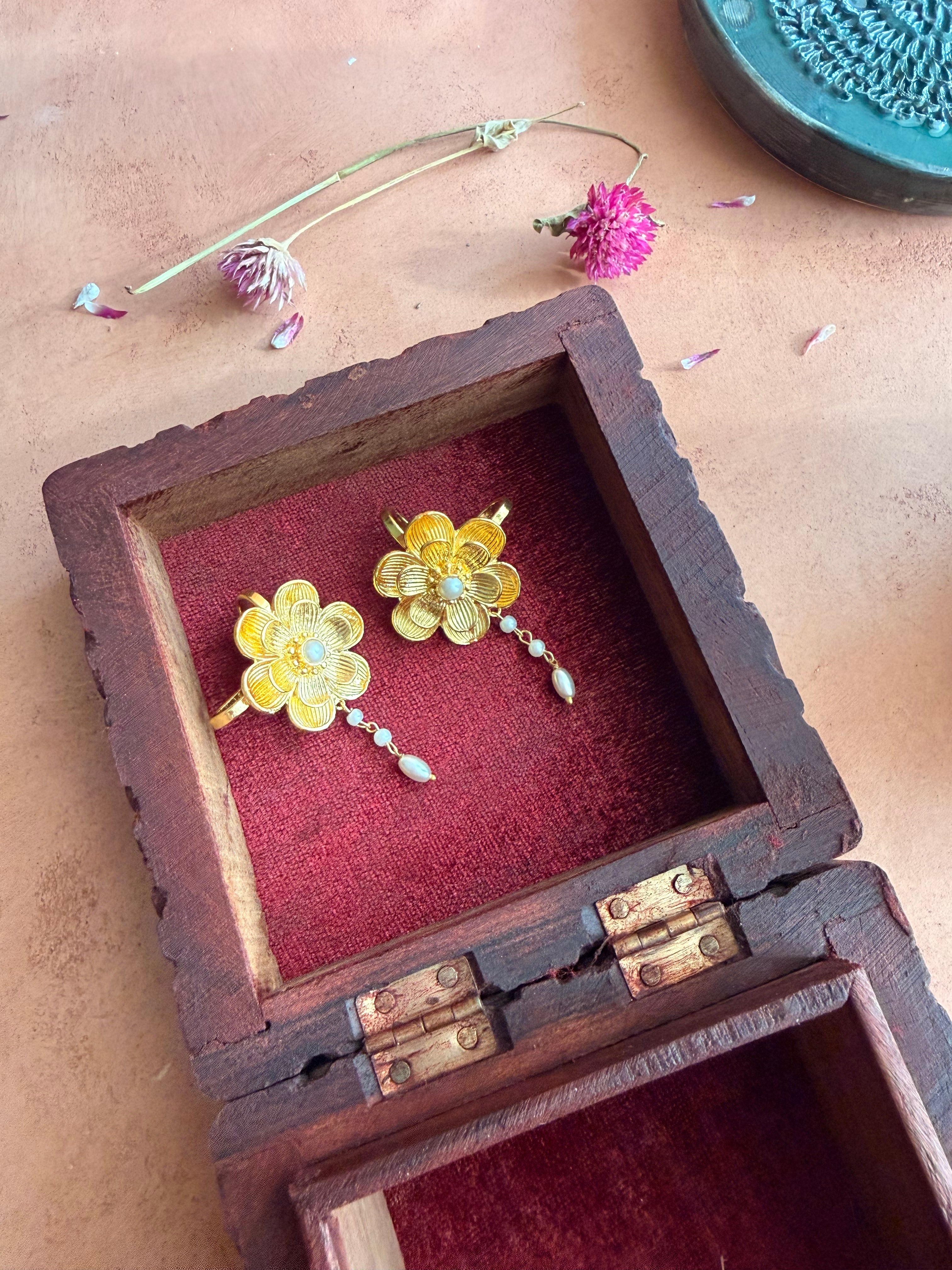Nargis Ear Cuffs nestled inside an antique wooden box with red velvet lining, gold flower and pearl drop visible, dried flowers and petals on terracotta surface around it
