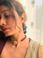 Woman in a cream sequined saree wearing the Nargis Mala necklace and matching ear cuff, looking down beside a sheer curtain.